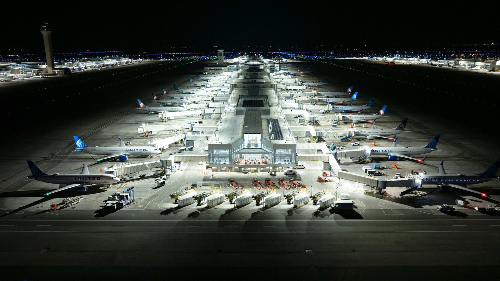 Aerial night view of a Denver International Airport concourse with United Airlines aircraft at the gates, lit by apron and gate lighting